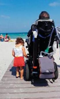 Persona con disabilità in carrozzina fotografata di spalle, insieme a una bambina, verso la riva del mare