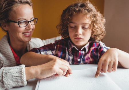 Un'assistente all'autonomia e alla comunicazione insieme a un bimbo con disabilità visiva