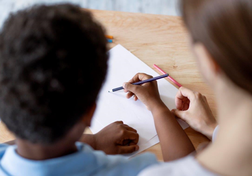 Bimbo di spalle insieme a donna che lo aiuta a scrivere