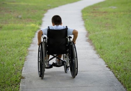 Ragazzo con disabilità in carrozzina sul vialetto di un parco