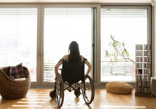 Donna con disabilità in carrozzina fotografata in casa di spalle
