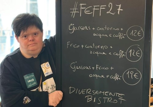 Lavoratrice di "Diversamente Bistrot", a fianco della tabella con il menu
