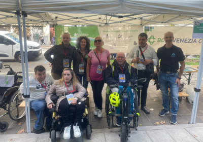 In primo piano, da destra, Giampiero Licinio, presidente della FISH Friuli Venezia Giulia, Alessandra Ferletti, presidente della UILDM di Gorizia e Massimiliano Mauri, altro componente di quest'ultima Associazione, davanti ad alcuni volontari presenti a "Gusti di Frontiera 2025"