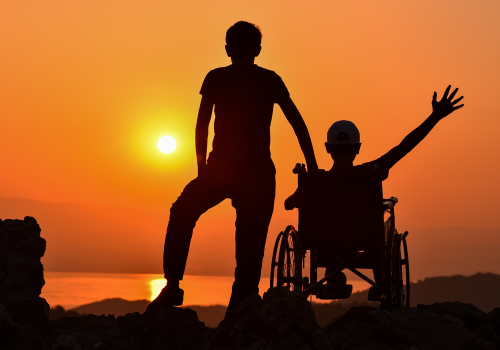 Adulto e figlio con disabilità in carrozzina davanti al sole che sorge