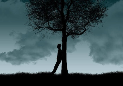 Uomo in ombra che riflette appoggiato a un albero