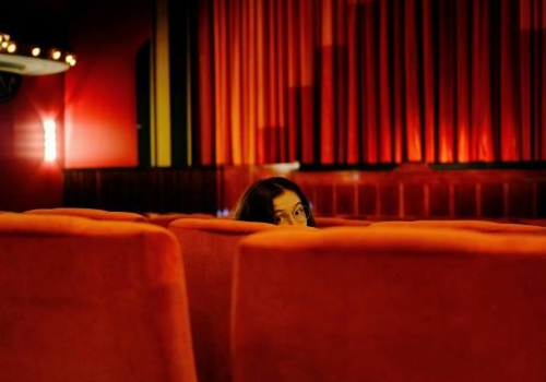 Testa di ragazza con gli occhiali che spunta dalla poltrona rossa di un cinema