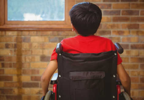 Ragazzo con disabilità in carrozzina fotografato di spalle davanti a una finestra