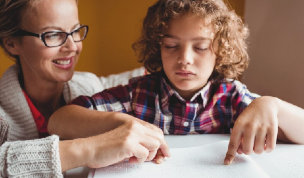 Un'assistente all'autonomia e alla comunicazione insieme a un bimbo con disabilità visiva