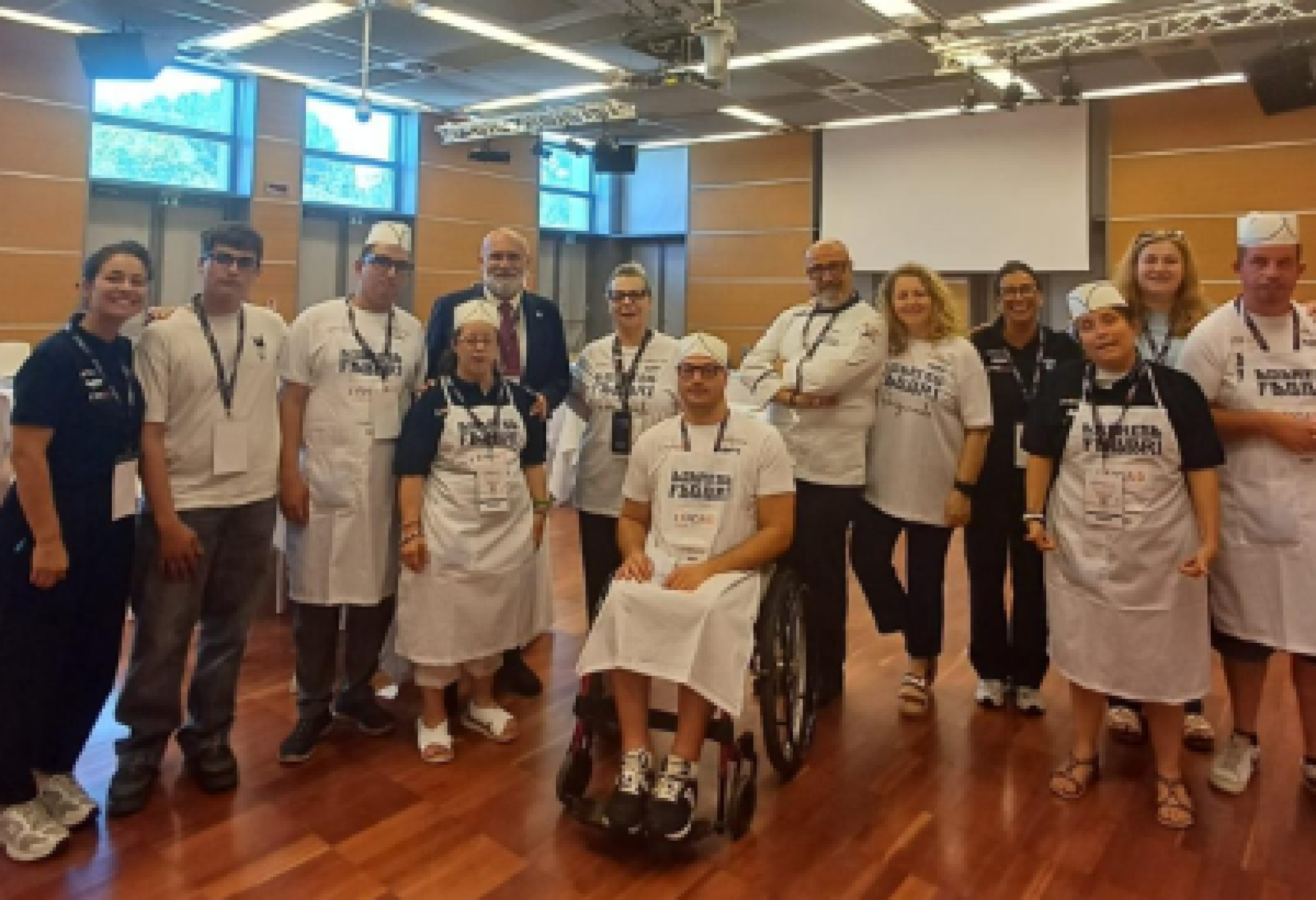 Il team di "Frolleria ANFFAS Mirandola" a "ExpoAid 2026", con Carlotta Fabbri, quinta generazione di Fabbri 1905 (prima a sinistra), Roberto Speziale, ppresidente nazionale dell'ANFFAS (quarto a sinistra, dietro), il pasticciere formatore Domenico Costanza (sesto da sinistra, dietro) e Marzia Manderioli, presidente dell'ANFFAS di Mirandola (ottava da sinistra, dietro)