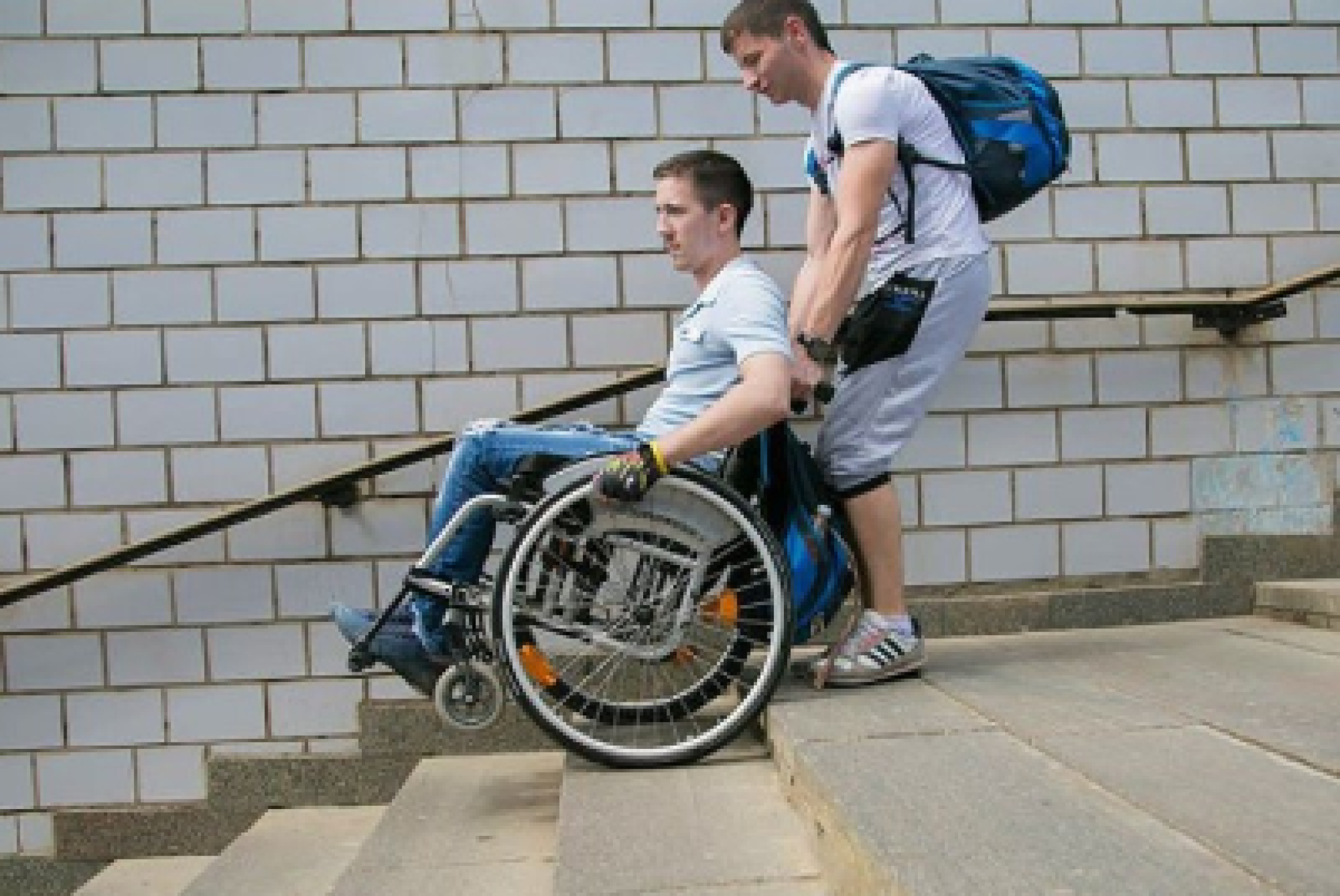 Un giovane in sedia a rotelle affronta una rampa di scale con l’aiuto del suo assistente personale
