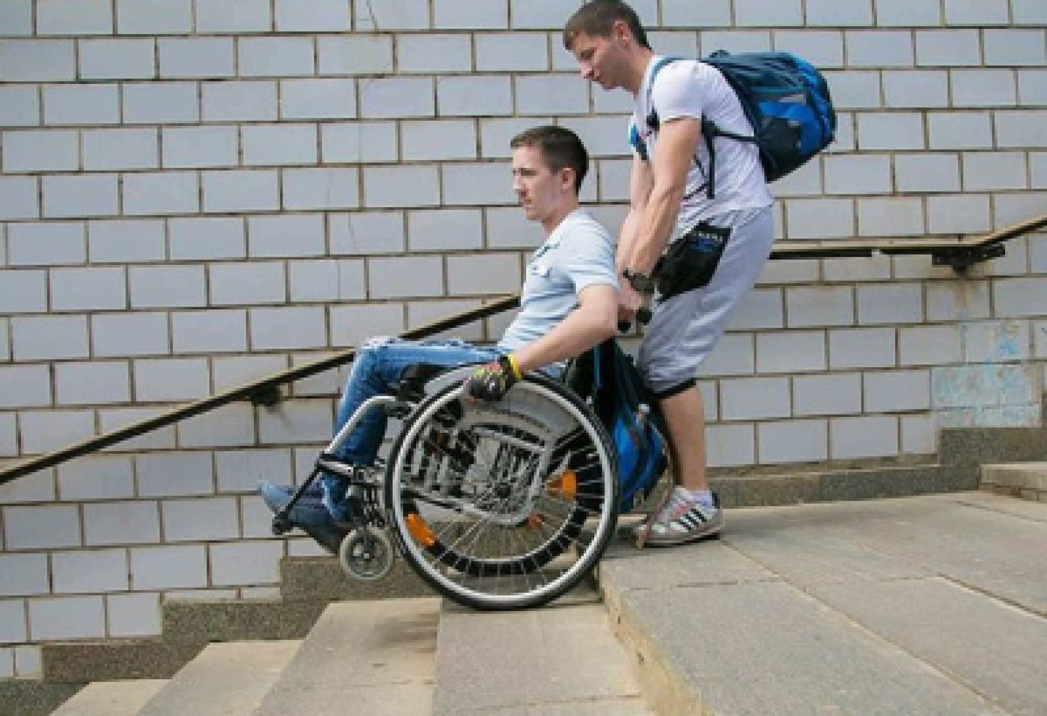 Un giovane in sedia a rotelle affronta una rampa di scale con l’aiuto del suo assistente personale